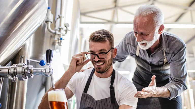 Old man teaching a young man on how to serve a beer