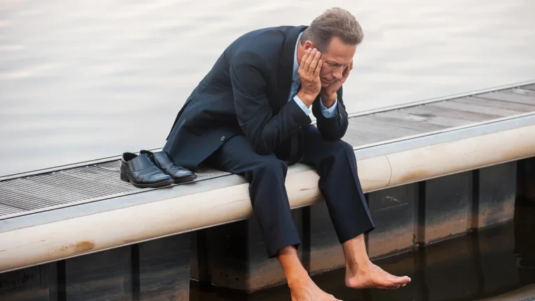 A man barefooted with his shoes on his side while seating on bench because of emotional cost in wrong business mindset
